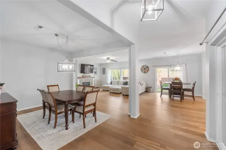 An open, airy floorplan with defined dining, living, and kitchen spaces, all tied together by wide-plank hardwood flooring. Clean sightlines stretch from the front living areas to the back of the home, emphasizing the home’s spacious feel and easy day-to-day flow.
