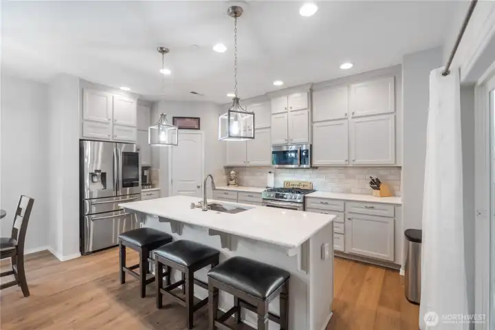 A beautifully updated kitchen with soft white cabinetry, quartz countertops, and a spacious island with seating for three. Stainless steel appliances, subway-tile backsplash, and upgraded lighting create a clean, modern look. This is a true centerpiece of the home with plenty of prep space and huge pantry.