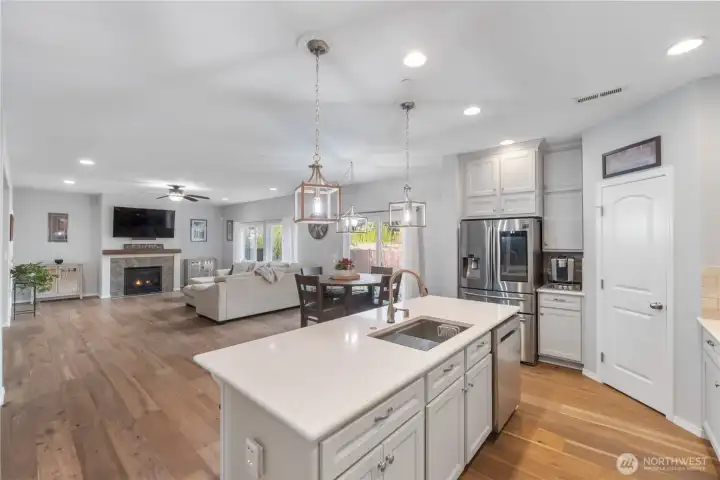 A wide, open view from the kitchen into the living and dining areas, showing how seamlessly the spaces connect. The island anchors the room, while large windows and recessed lighting keep everything bright throughout the day. Perfect for staying connected whether cooking, hosting, or relaxing.