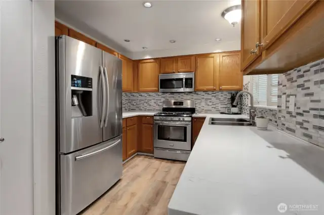 Functional galley-style kitchen featuring stainless steel double sink, all stainless appliances, sleek Corian countertops, and warm laminate wood flooring.  A pantry closet adds extra storage.
