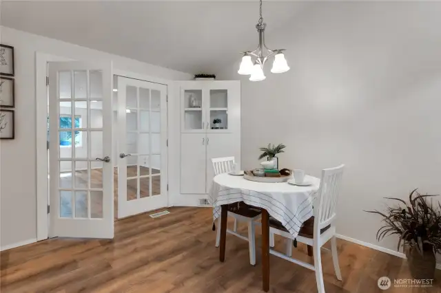 Dining area just off the kitchen, featuring matching laminate flooring, French doors that open to the expansive great room, and a charming corner cabinet with glass front upper doors perfect for displaying dishes, glassware, or keepsakes, with addioinal stoarge below