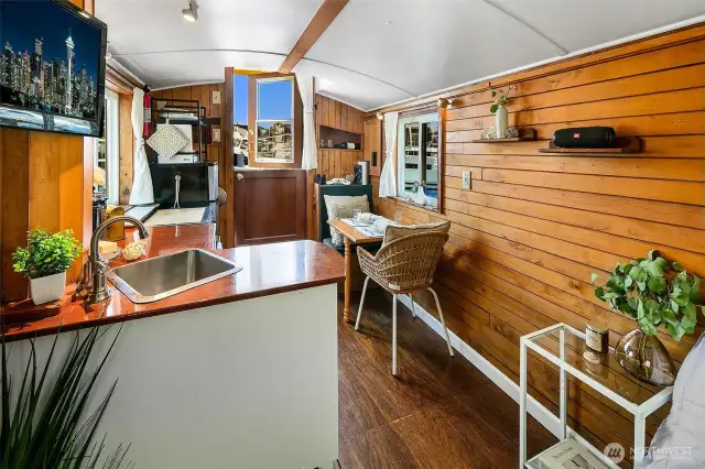 The saloon flows from galley to mess, wrapped in warm wood paneling and lit by double-pane windows, with the aft door opening to Lake Union’s sparkling water and fresh air.