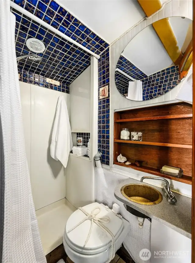 The bright head features a tiled shower and an upgraded electric macerating Dometic marine toilet, paired with open shelving for easy storage and warm wood accents.