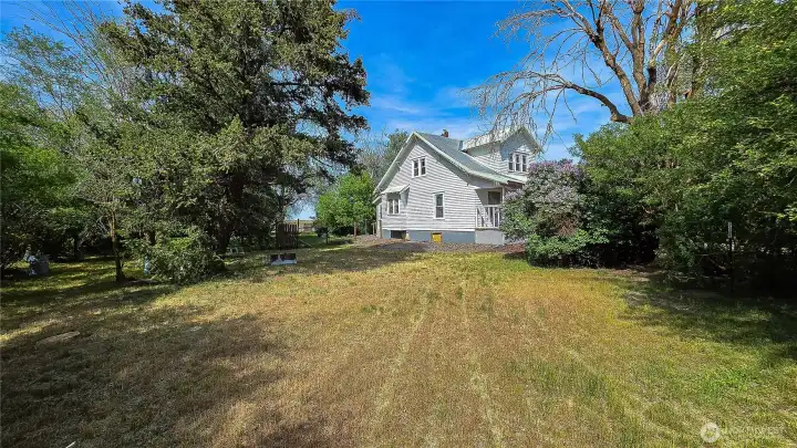 Side exterior view highlighting the large yard, established landscaping, and a blooming lilac bush next to the home. Looking East from the west side of the home.