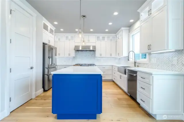 Designer kitchen outfitted with high-end Dacor appliances, quartz countertops, large island & herringbone tile backsplash.