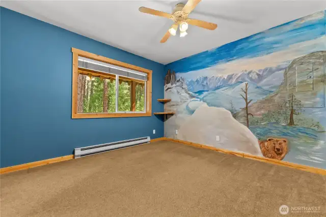 Main floor bedroom:    Large window frames peaceful forested views and natural light    Custom wall mural adds artistic flair with a scenic mountain landscape