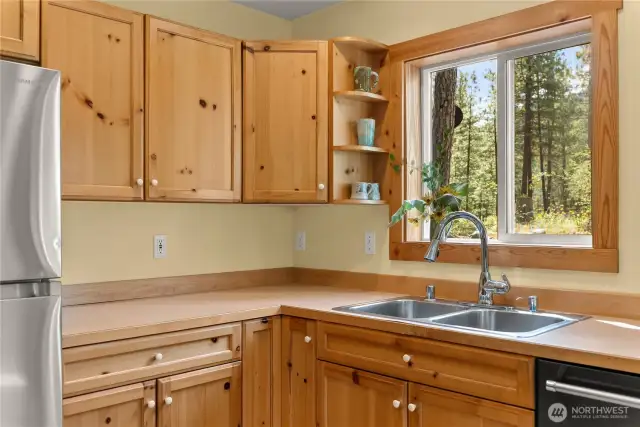 Deep stainless sink perfectly positioned beneath a bright window.    Open shelving and spacious counters offer functionality and rustic charm