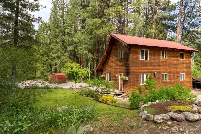 Well-maintained yard with established garden beds and lush lawn.  Detached storage shed with matching roof for tools or gear.