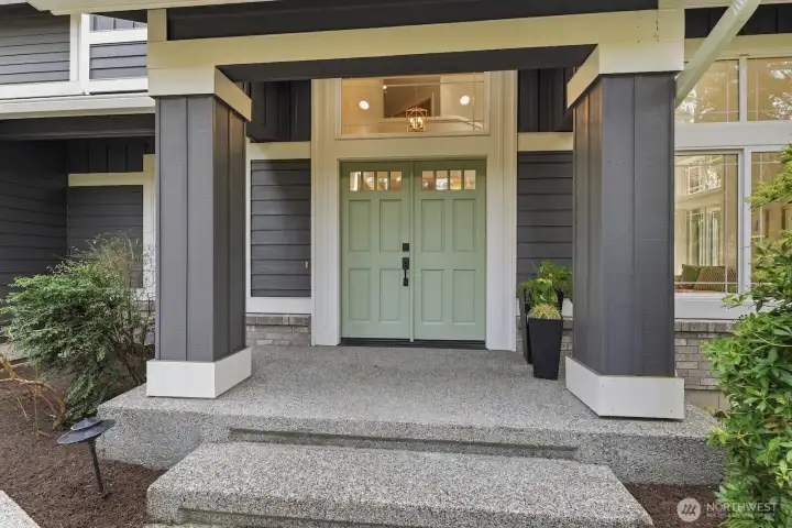 Grand covered entry porch framed by beautifully maintained landscaping, creating warm and welcoming curb appeal.