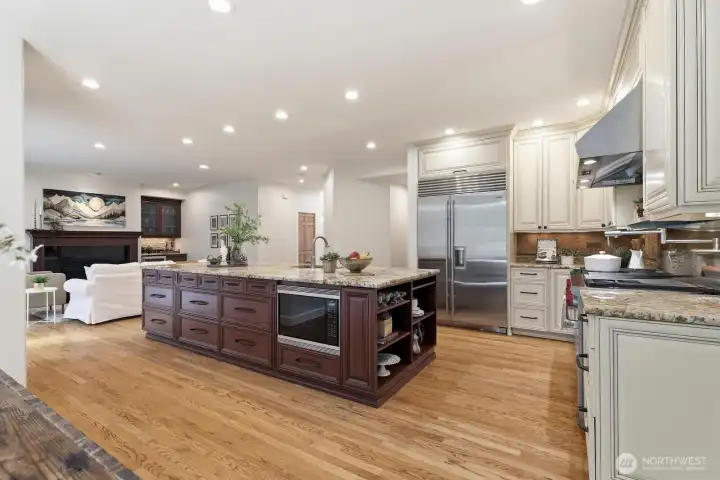 Gourmet kitchen featuring under-cabinet lighting, slab granite countertops, custom cabinetry, an expansive island, walk-in pantry, tiled backsplash, and a pot-filler.