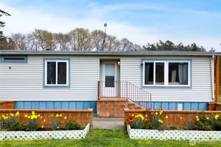 Charming front exterior with a welcoming entry, brick accents, and landscaped flower beds. The home’s clean lines and neutral tones enhance curb appeal in a serene country setting.