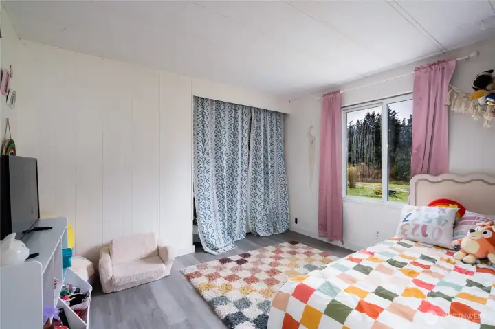Bright and cheerful secondary bedroom with large windows, colorful decor, and ample space for furniture. Ideal for a child’s room or flexible living space.