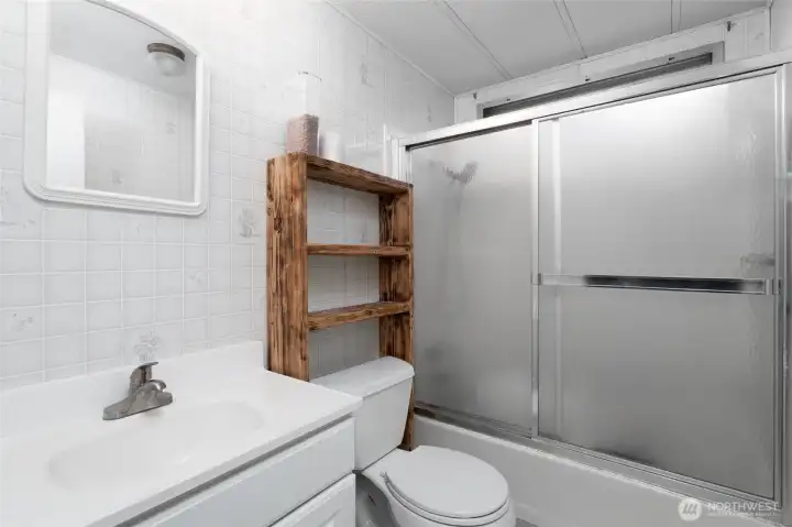 Well-appointed bathroom with a shower/tub combo, clean white vanity, and additional shelving for storage. Practical layout for everyday use.