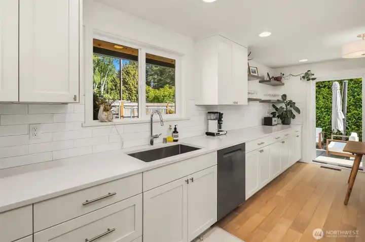 Bright, light-filled kitchen with quartz counters, undermount sink, stainless steel dishwasher, recessed lighting, and expansive prep space overlooking the backyard.