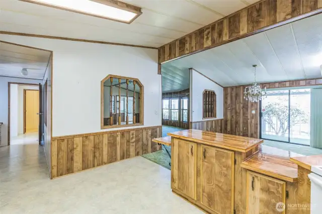 Opposite side of the eating bar standing in the kitchen. To the left is a hallway with a built-in desk area leading to and from the laundry/mudroom and full bath.