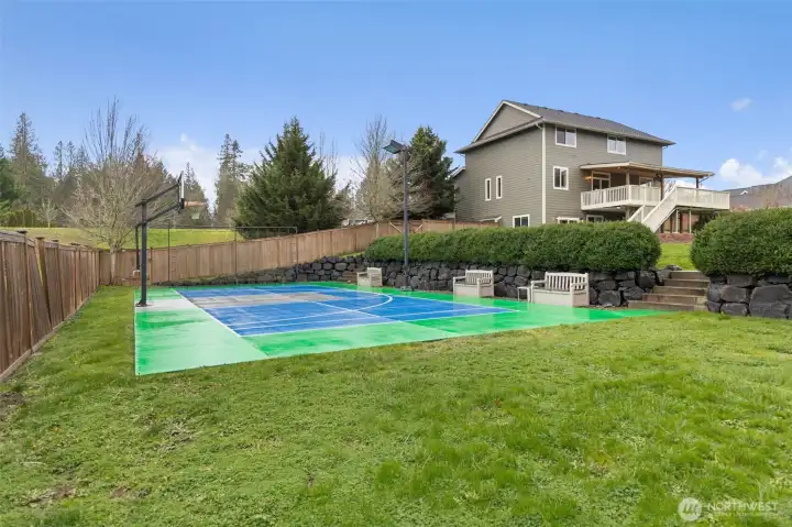 This outdoor setup is ready for action! A dedicated sports court anchors the lower level of the fenced backyard, complete with a basketball hoop and plenty of space to move. Elsewhere in the backyard, a gravel zone previously held a batting cage, giving you flexibility for training, play, or creative outdoor uses. The tiered layout continues with steps leading up through established landscaping and terraced hardscaping, creating a backyard that feels layered, functional, and thoughtfully designed for both play and relaxation.
