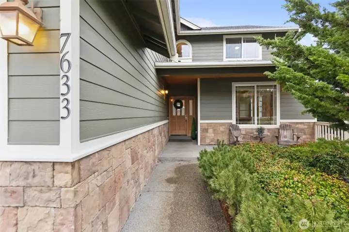 This approach to the front door feels welcoming right away and just out of sight is a lovely water fountain. The walkway runs neatly along the garage wall, leading you past stone accents along the lower half of the home and lap siding above, all finished in a soft sage green with crisp white trim. The covered front porch sits right in front of the den or parlor window, creating the perfect spot for a couple of chairs, morning coffee, or just watching the neighborhood go by. Ring doorbell camera stays too!