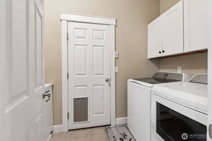 Laundry feels refreshingly functional here in this main floor setup, which includes white shaker cabinets for storage, space to expand along the side wall, and tile floors that handle real life without complaint. The washer and dryer are included, so you’re ready from day one, plus a pet door built into the garage entry adds a thoughtful touch that makes daily routines easier, especially for anyone juggling paws and people at the same time.