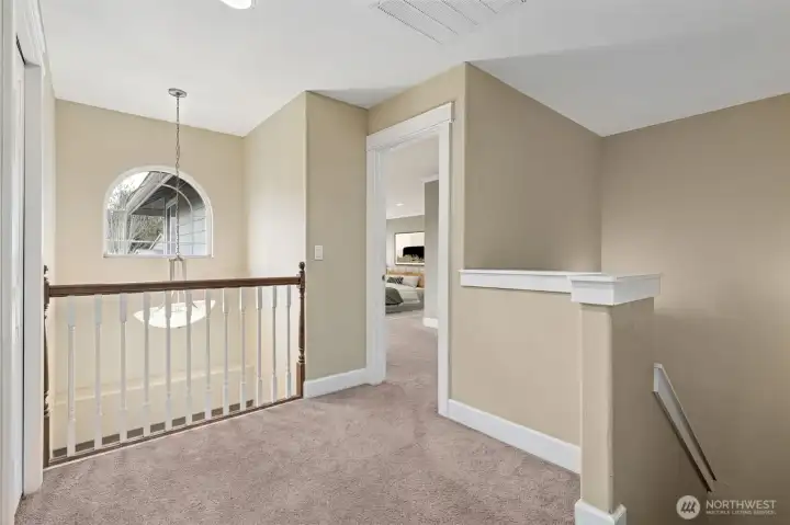The top of the stairs shows the two story entry foyer arched window and overlook balcony style loft space, with an open area between the upstair rooms. Soft carpeting for comfort and less walking noise too.