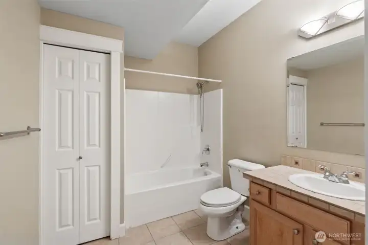 In this downstairs level full bathroom, there is plenty of space to move around, a tub surround that’s clean and practical, and a solid wood shaker vanity in a warm medium tone that adds some weight to the room. Tile floors keep things durable, while the soft muslin wall color and crisp white trim keep it feeling pulled together. Add in a linen closet with classic six panel doors and this bathroom is fully equipped for guests, movie marathons, and everyday use downstairs.