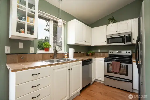 Stainless appliances and tile countertops, durable & water resistant flooring extends from the kitchen into adjacent living spaces for ease of cleaning and cohesive design.