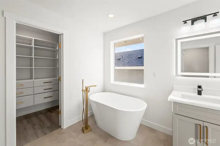 Soaking tub and generous walk-in closet featuring lovely built-ins