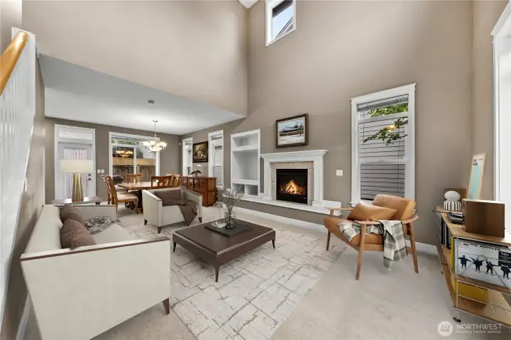 Bright and inviting living room with soaring cathedral ceilings, expansive windows, and abundant natural light. The gas fireplace with elegant mantel creates a warm focal point, while the open layout flows seamlessly into the dining area, making the space feel both spacious and welcoming. Bright and inviting living room with soaring cathedral ceilings, expansive windows, and abundant natural light. The gas fireplace with elegant mantel creates a warm focal point, while the open layout flows seamlessly into the dining area, making the space feel both spacious and welcoming.