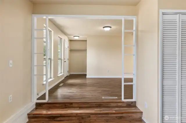 The framed arch of the transition between the living room and family room shows the entry foyer, with open closet space perfect for a future foyer bench over shoe storage spot.