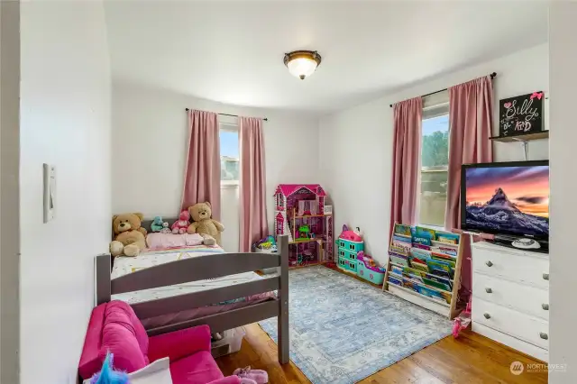 Bedroom #3, facing the front of the home, showcases its original hardwood flooring and is bathed in natural light streaming through the vinyl windows.