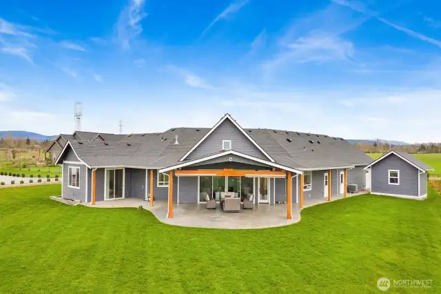 Beautiful back view picture featuring the large, covered patio with stamped concrete and plumbed for an outdoor kitchen, gas fireplace, and hot tub. Sliders on the left lead to your primary ensuite.