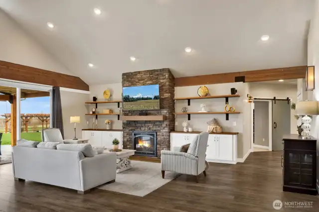 This living area photo nicely displays the custom built-ins and shelving that were created to display all your art, photos, and showpieces. In the distance is the primary ensuite featuring barn doors that were added to several rooms throughout the home.