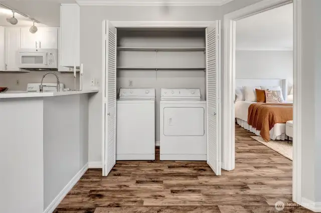 In-unit laundry with storage shelves in closet between kitchen and primary bedroom