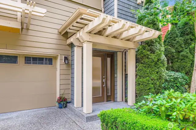 Trellis awning adorns the front porch. Shingled exterior. Mature landscaping.