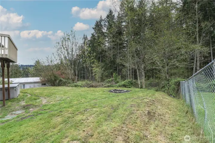 Expansive backyard with a firepit area, mature trees, and a peaceful greenbelt backdrop. Fully fenced and ideal for outdoor gatherings, play, or relaxing in a natural setting.