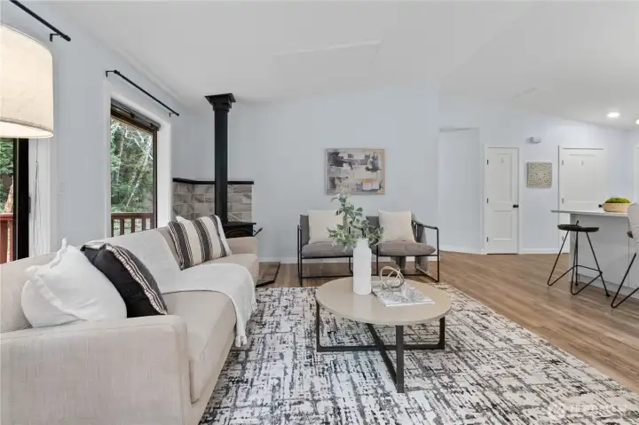 Living room and dining area with wood stove and multiple windows for natural light