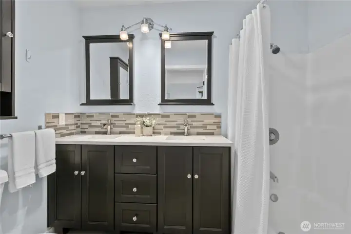 Bathroom with double vanity, solid surface counters, and tub/shower combination