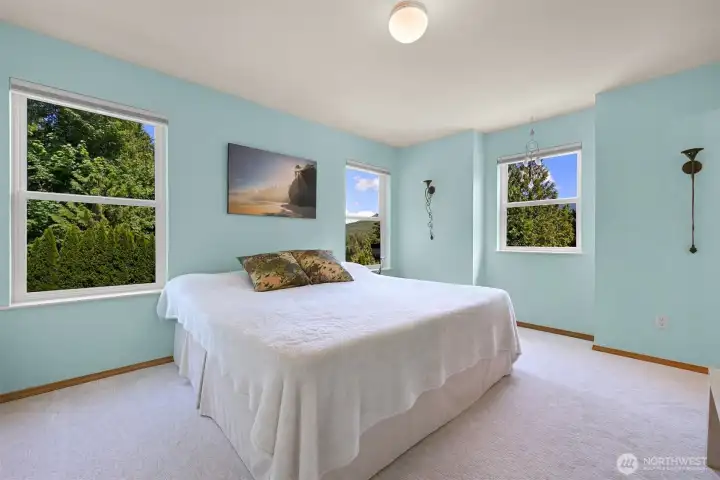 The spacious primary bedroom enjoys windows on two walls, filling the room with natural light and views of the surrounding forest, gardens, and the iconic Twin Sisters Mountains. It's a peaceful retreat that reflects the property's connection to nature. The spacious primary bedroom enjoys windows on two walls, filling the room with natural light and views of the surrounding forest, gardens, and the iconic Twin Sisters Mountains. It's a peaceful retreat that reflects the property's connection to nature.