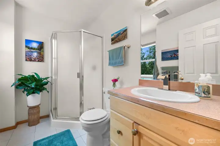 The primary bath features a walk-in shower, natural light, and a functional layout that serves the primary suite. A large window brings in views of the surrounding trees while maintaining privacy. The primary bath features a walk-in shower, natural light, and a functional layout that serves the primary suite. A large window brings in views of the surrounding trees while maintaining privacy.
