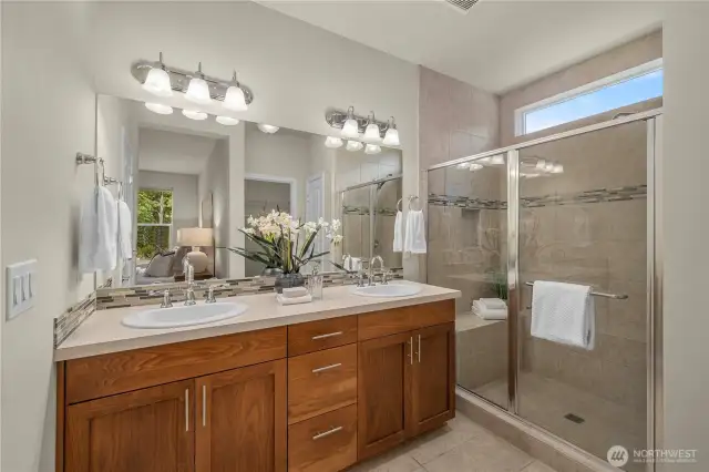 Primary bathroom offers dual sinks, tile floors and tiled shower with a bench and a handy niche.