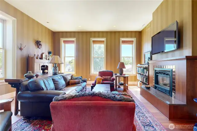 Warm and inviting living room with tall ceilings, abundant natural light, and a beautifully framed gas fireplace