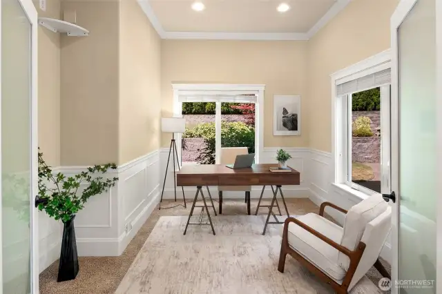 A glass French door opens to a beautiful office with garden views, wrapped in elegant wainscoting.
