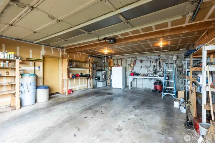 Spacious garage with extra refrigerator, workbench, and solid shelving
