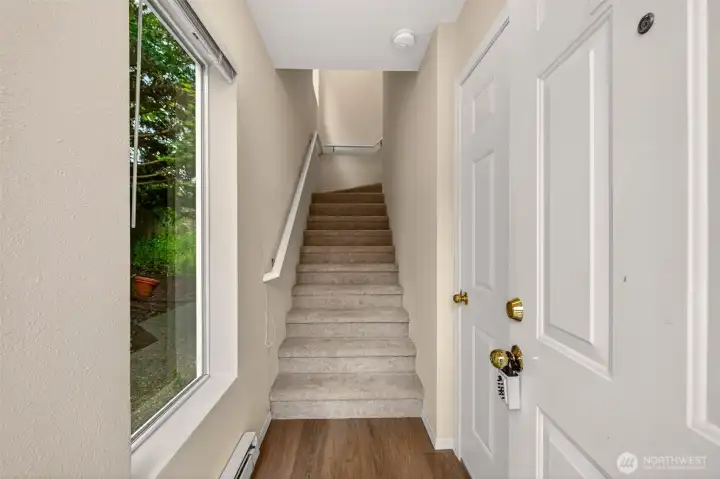 A bright, welcoming foyer with a window framing lush greenery sets a calm tone the moment you step inside. The staircase leads up to the home's single-level top-floor living, where new flooring carries you into the heart of the home.