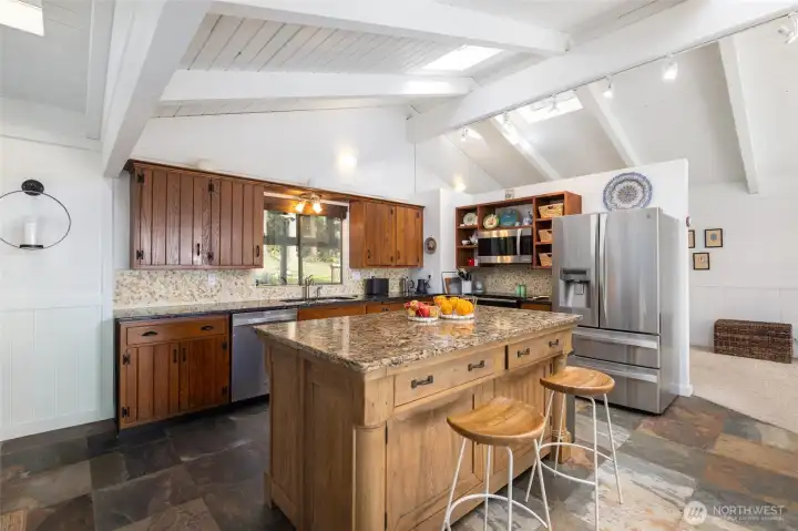 The expansive kitchen reflects woodland tones and textures from the surrounding landscaping, as reflected in the handsome granite countertops, pebble backsplash and rich, wood-stained cabinetry with display shelves.
