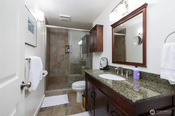 The lower level primary bath, off the large bedroom suite, has been handsomely remodeled with glass doors, tiled shower, granite vanity countertops, and more.