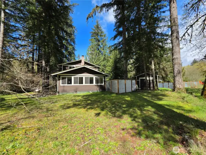 Even wider sunny view of the house, shed and fenced yard.