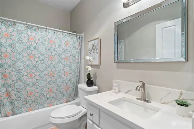 Newly renovated hall bath with full tub and shower, new toilet, fixtures, and countertop.