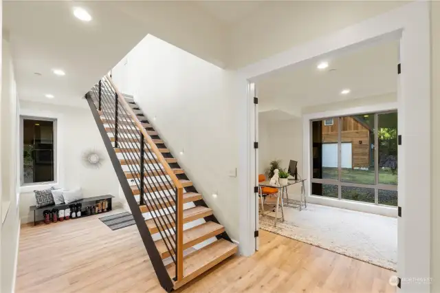 A gorgeous floating staircase with in-wall lighting and cork stair treads accentuates the mudroom entrance from attached garage .