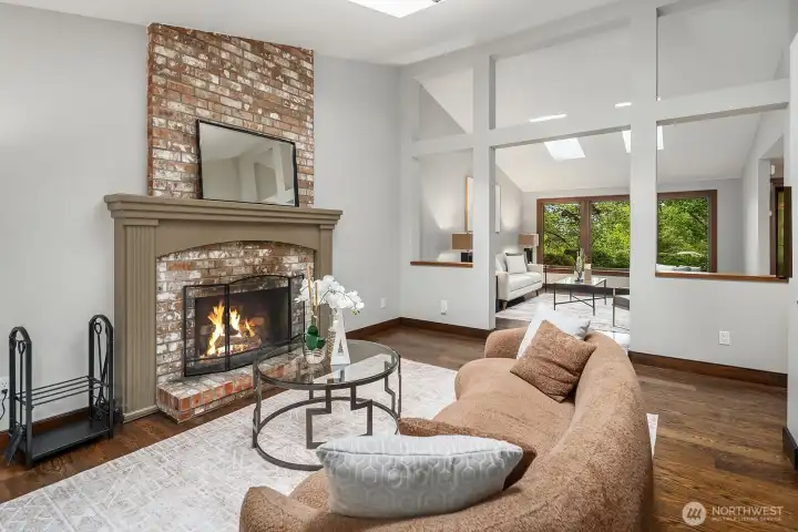A stunning stone fireplace anchors this cozy sitting area, offering a warm and inviting focal point framed by vaulted ceilings and views of the lush natural surroundings beyond.