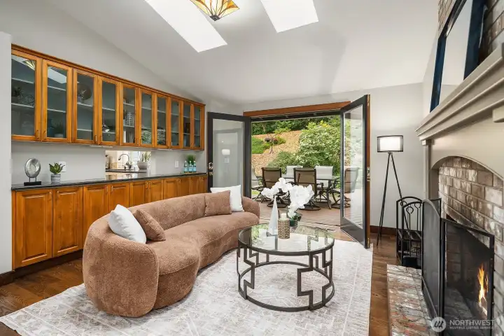 Another view of the beautiful stone fireplace and sitting area showcases the skylights, warm natural light, and French doors that open to the expansive deck and serene greenbelt beyond.